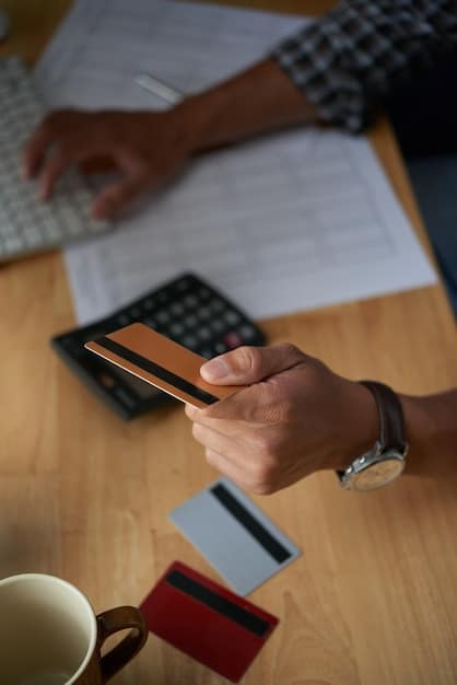 A close-up shot of a hand holding a credit card, with a calculator and various bills blurred in the background. This image represents the impact of interest rate hikes on consumer spending and debt.