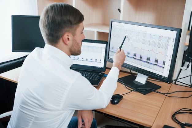 A person analyzing a complex data chart on a computer screen in a modern office environment. There are multiple monitors displaying various data points.