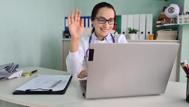 A doctor is smiling and waving during a telehealth appointment on a laptop screen. The background is a blurred image of a modern clinic, subtly indicating the professional nature of the virtual consultation.